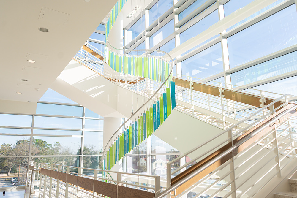 Curving ribbon of green and teal glass blades suspended past the atrium curtain wall