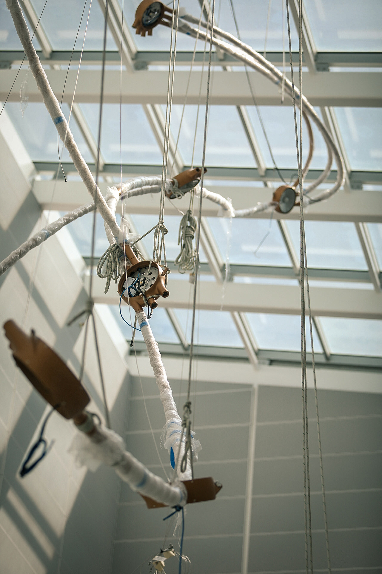 Protective-wrapped copper tubes and rigging ropes suspended beneath the atrium skylight