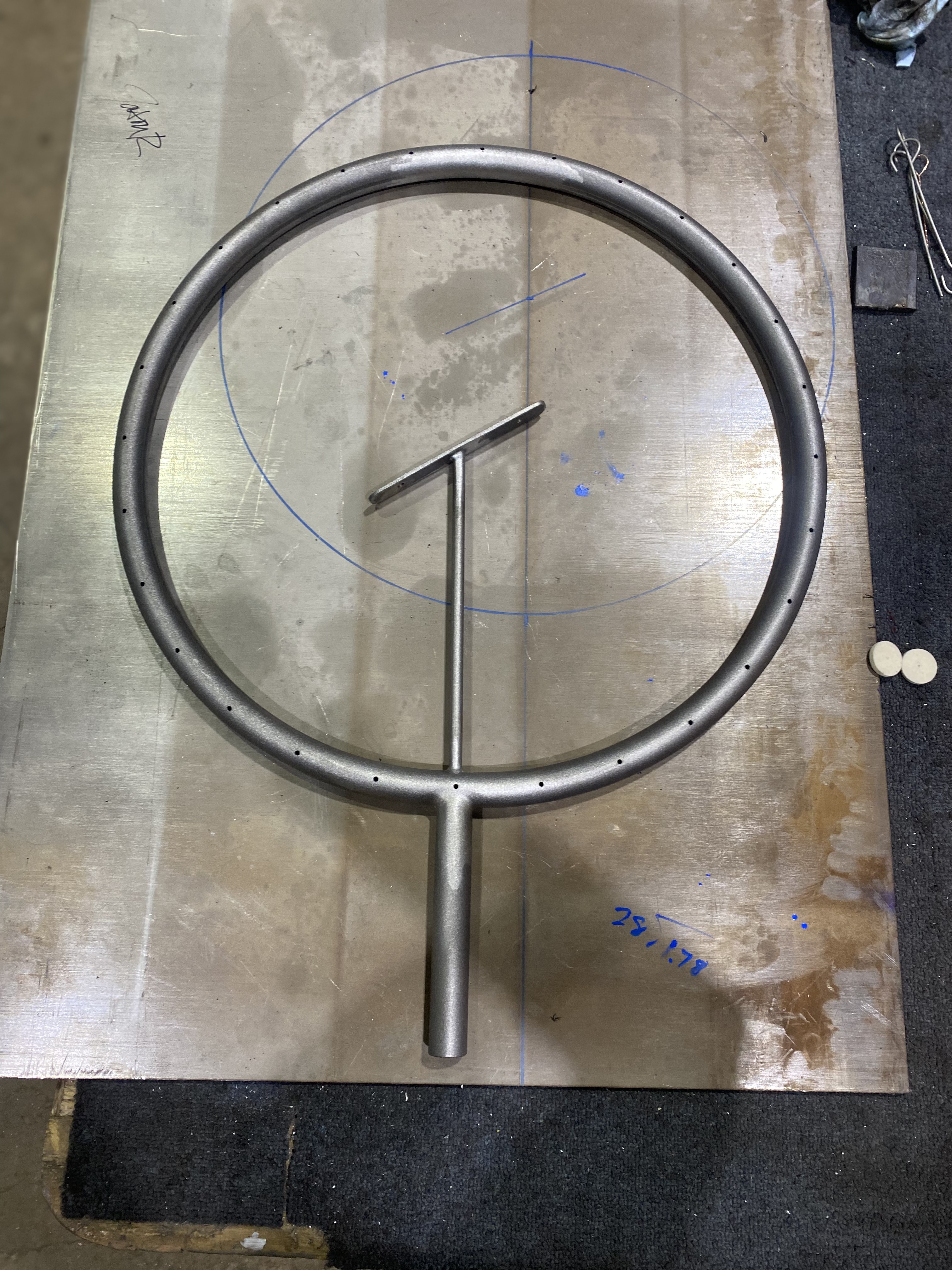 Machined and drilled tube ring with welded stem and mounting tab laid over its layout template