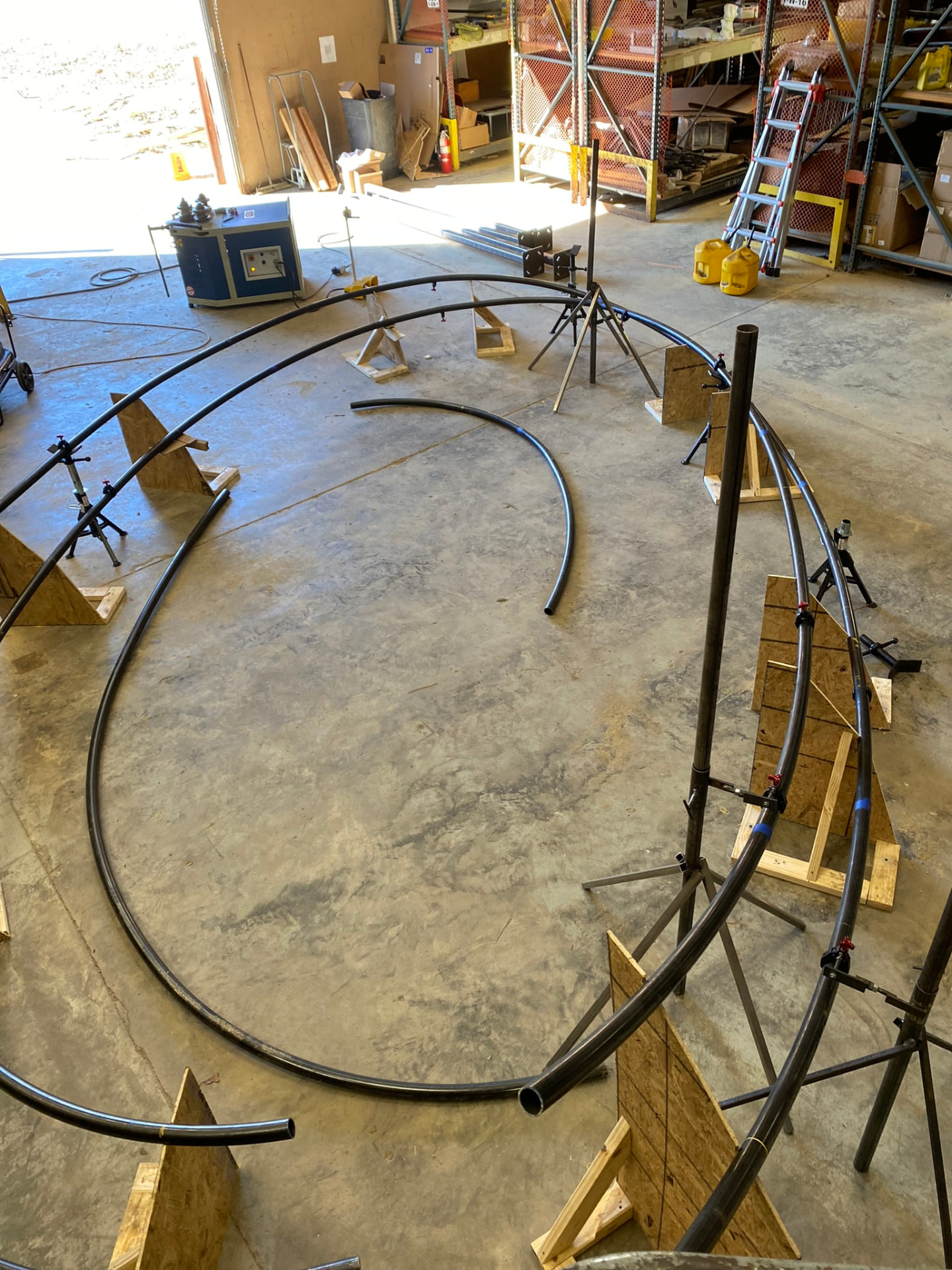 Trellis tube runners staged on pipe stands and plywood fixtures, forming the sweeping scroll profile