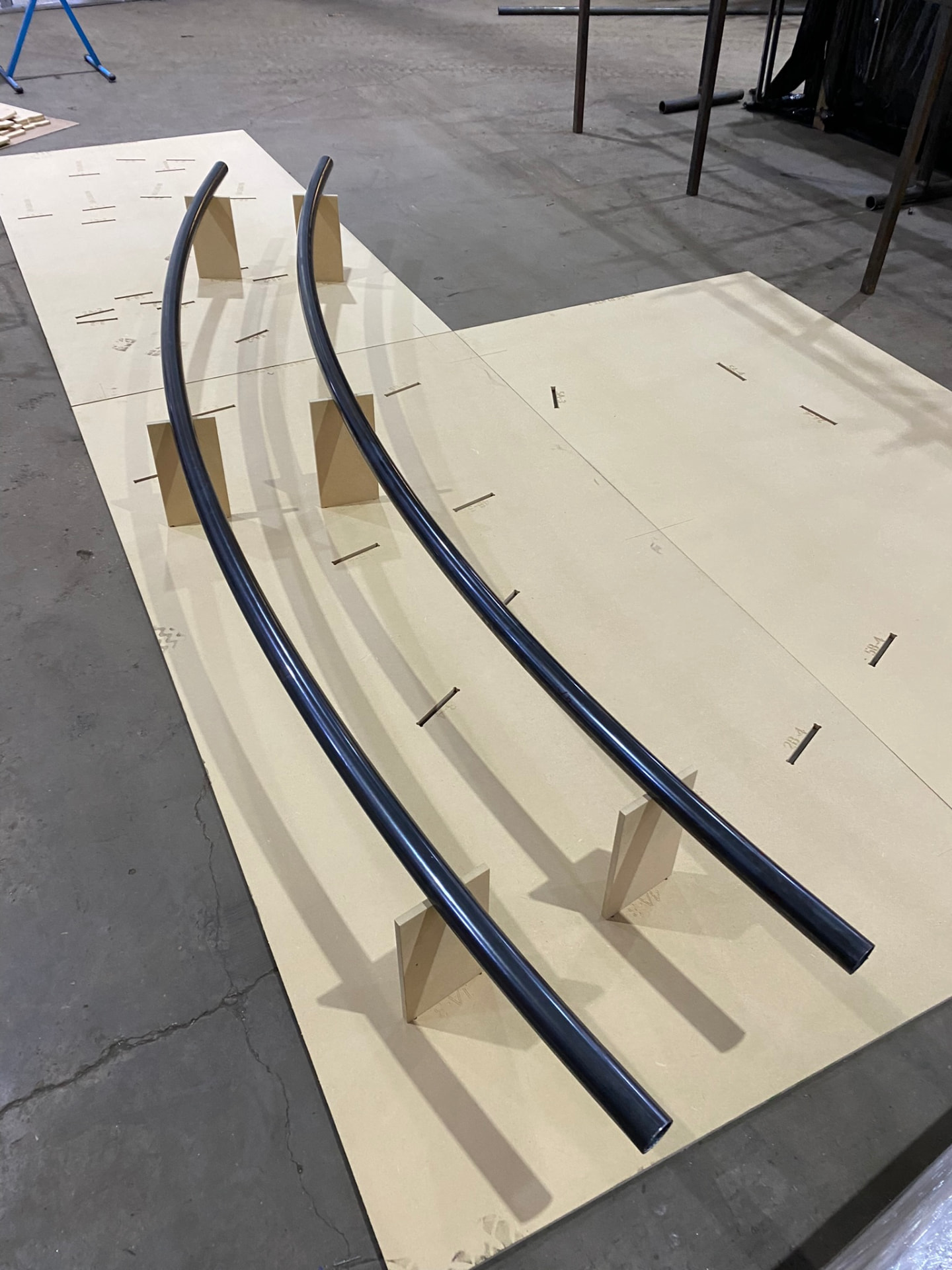 Two CNC-bent steel tube arcs checked against a full-scale CAD floor layout in the shop