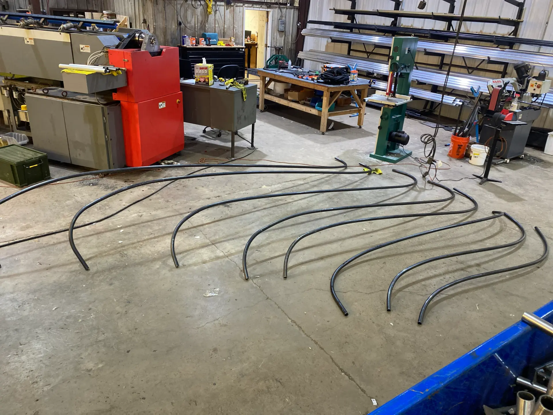 CNC bent freeform tube sections laid out on the shop floor beside the rotary draw tube bender
