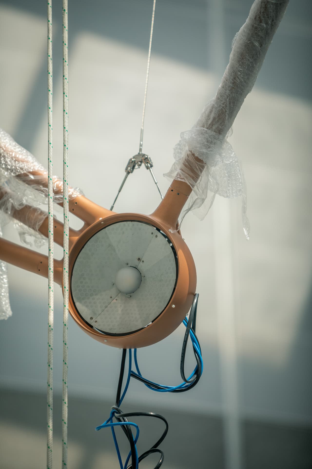 Star node lens assembly wrapped in protective plastic with rigging cables attached